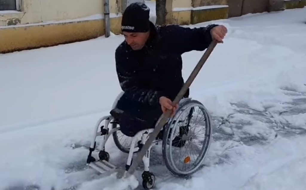 Imagini emoționante! Un bărbat în scaun cu rotile deszăpezește trotuarul din fața casei – VIDEO